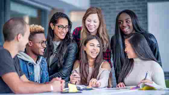 A diverse group of happy college students sitting around a table and talking with each other.