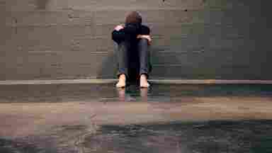 a girl curled up next to a wall.