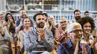 A crowd of diverse, happy people applauding someone after a presentation.