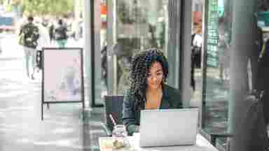 Ethnic young professional working from a laptop outside a modern street cafe.