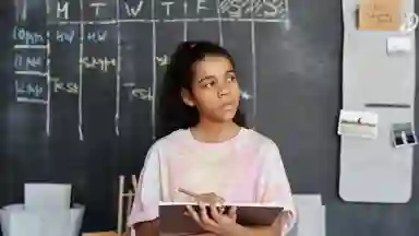 Person of color in pink and yellow crew neck t-shirt holding a brown notebook. 