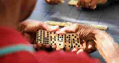 A retiree hides their hand while playing dominos with friends.