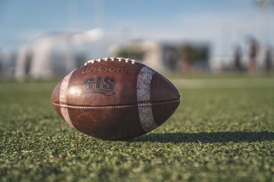 A football in focus on a playing field. Blurry shapes in the background