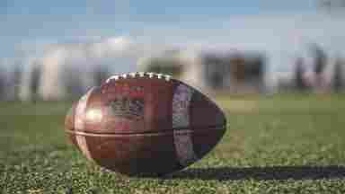 A football in focus on a playing field. Blurry shapes in the background