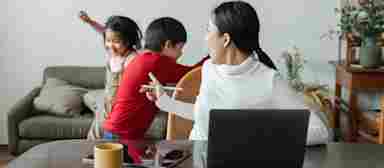 A young Asian woman works on a laptop and a tablet while trying to calm down active children.