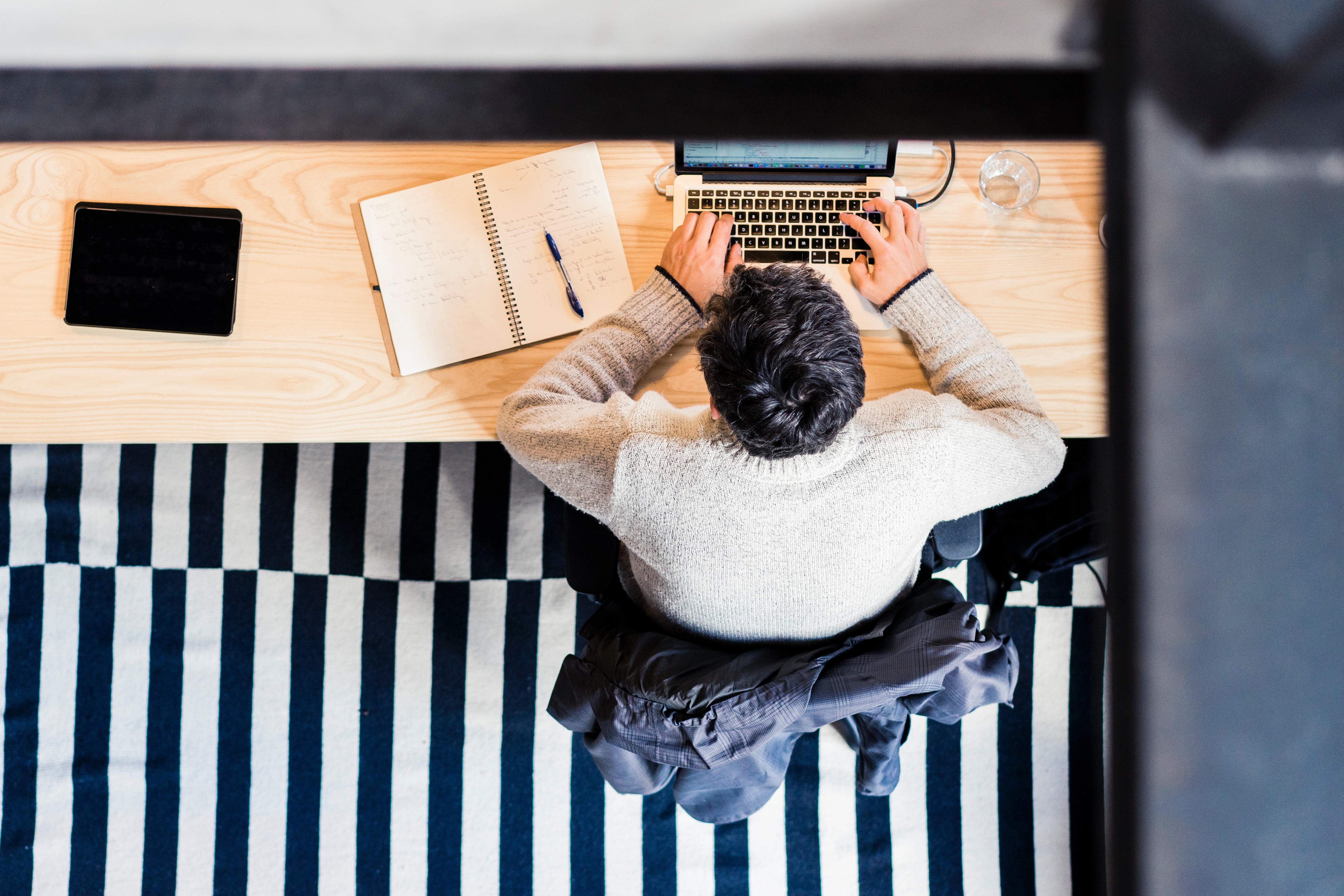 A person sits at a wooden desk and types on a small laptop. 