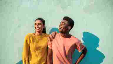 Two happy young adults, one woman and one man, looking to the left and smiling in front of a green-blue background.