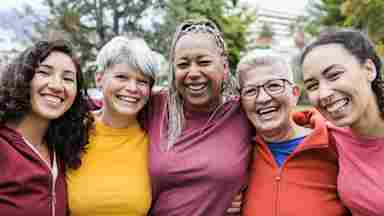 Group of smiling women standing shoulder-to-shoulder in nature.