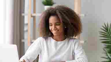 A happy Black teenage girl studying with a laptop and doing online research for a homework assignment.