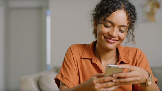 A young woman of color smiling as she accesses information on her smartphone.