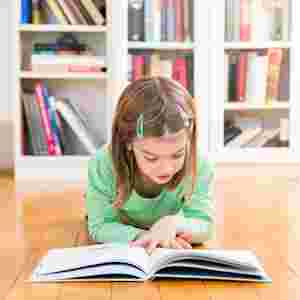Child in a green shirt laying on the floor and reading an open book