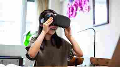 A happy young girl wears a virtual reality headset while sitting at her laptop.