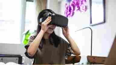 A happy young girl wears a virtual reality headset while sitting at her laptop.