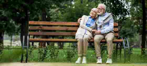 An elderly couple is sitting on a bench while holding each other in the park. Older. IStock#: 1151872303.