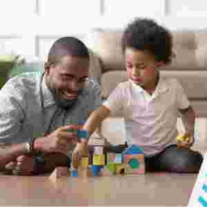 Caring young single father help cute kid son play on warm floor together, happy dad and little child boy having fun building constructor tower from colorful wooden blocks. IStock# 1158481694.