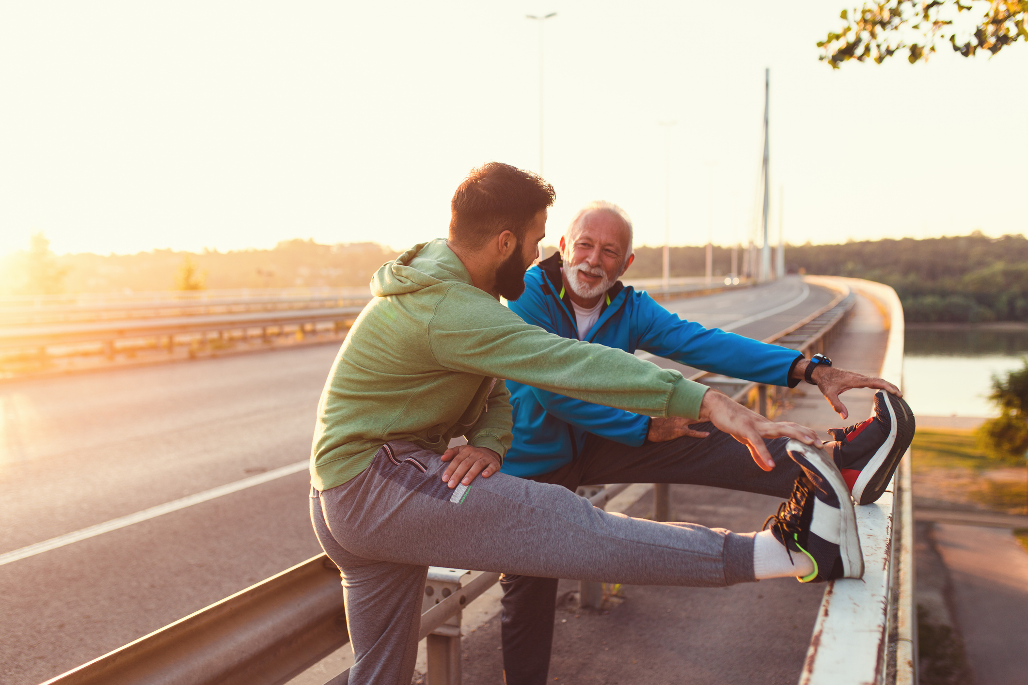 A father and son stop to stretch and encourage each other by the side of an exercise path. 