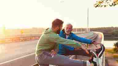 A father and son stop to stretch and encourage each other by the side of an exercise path.