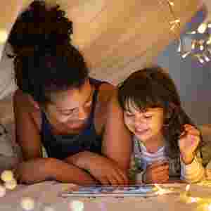 A mother and child reading in a cozy tent with hanging lights.
