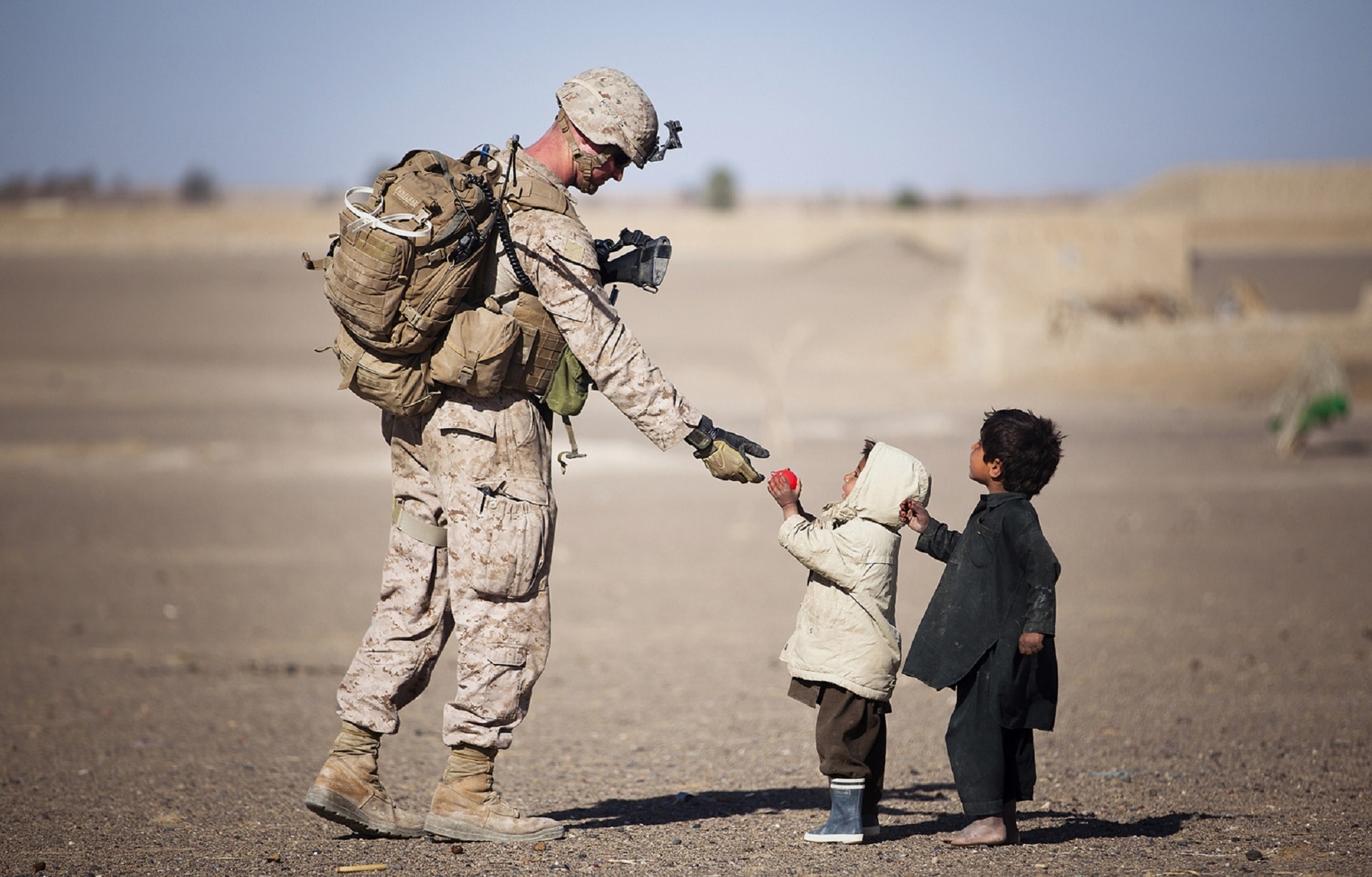 A soldier in the Middle East gives fruit to children during the daytime. 