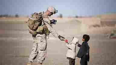 A soldier in the Middle East gives fruit to children during the daytime.