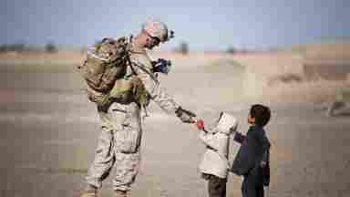 A soldier in the Middle East gives fruit to children during the daytime. 