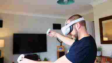 Man in a VR headset inside a living room, holding two VR controllers.