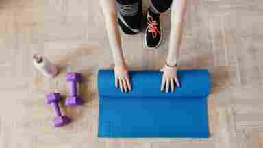 A person rolling up their blue yoga mat. Their water bottle and work out equipment is to their right.