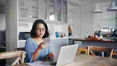 A young woman uses a smartphone and laptop to participate in brain strategy training.