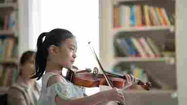 Nice little girl playing the violin for her parent sitting in sofa.