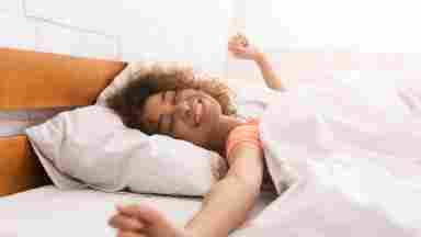 A happy woman stretching in bed with light gleaming down her face. 