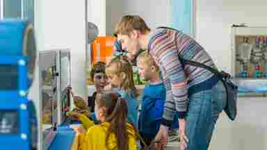 A group of kids of varied ages and genders explore a science exhibit together.