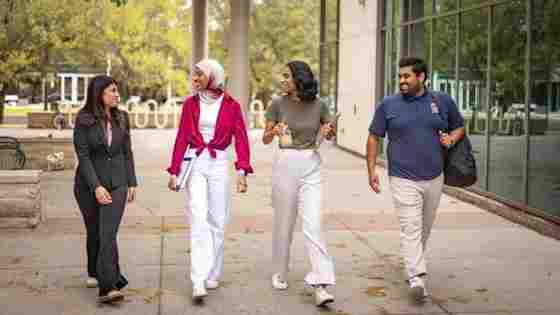 UT Dallas students in conversation while walking briskly across a green, placid campus.