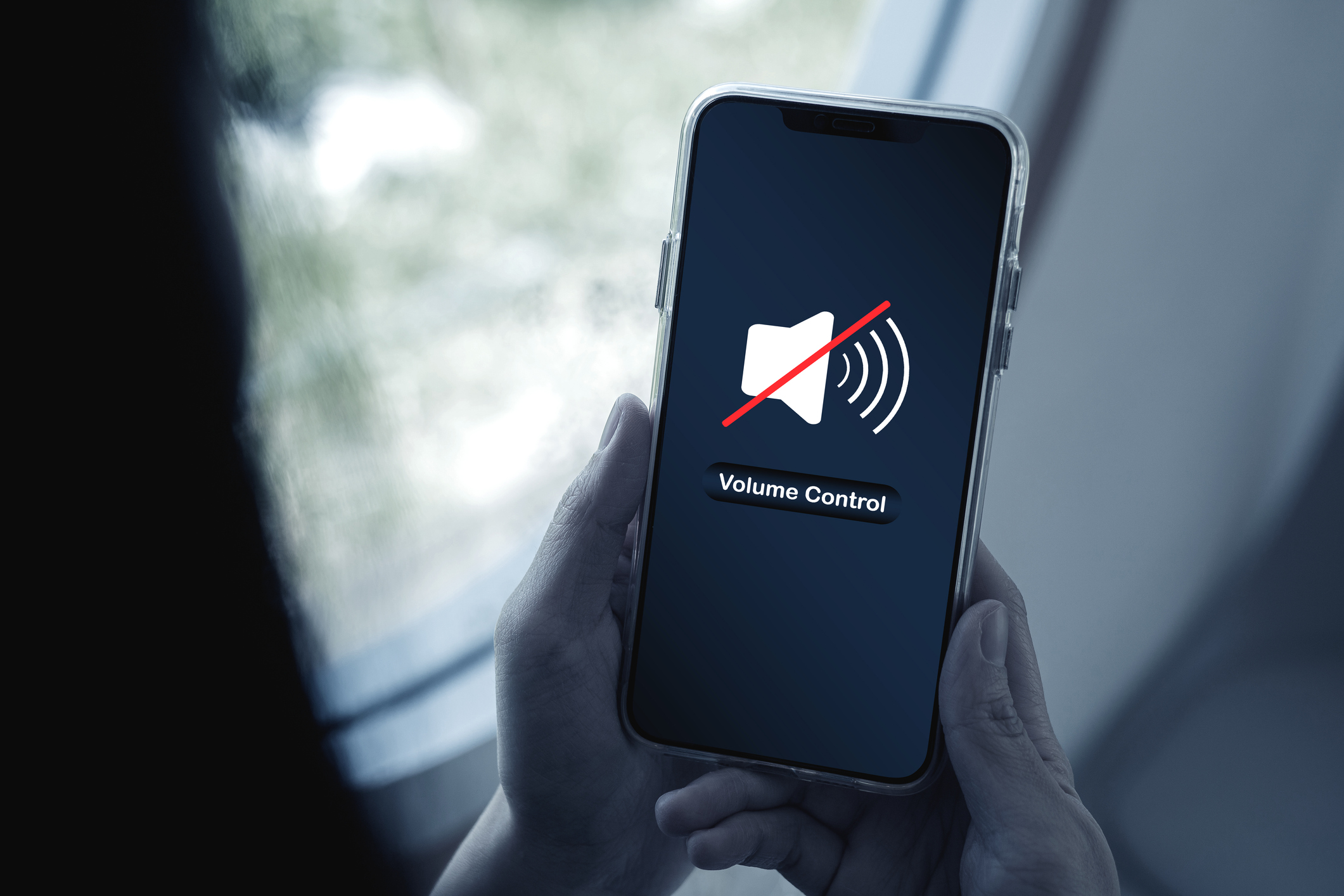 Hands holding a smartphone displaying a muted speaker icon with a red slash and the text "Volume Control" on screen.