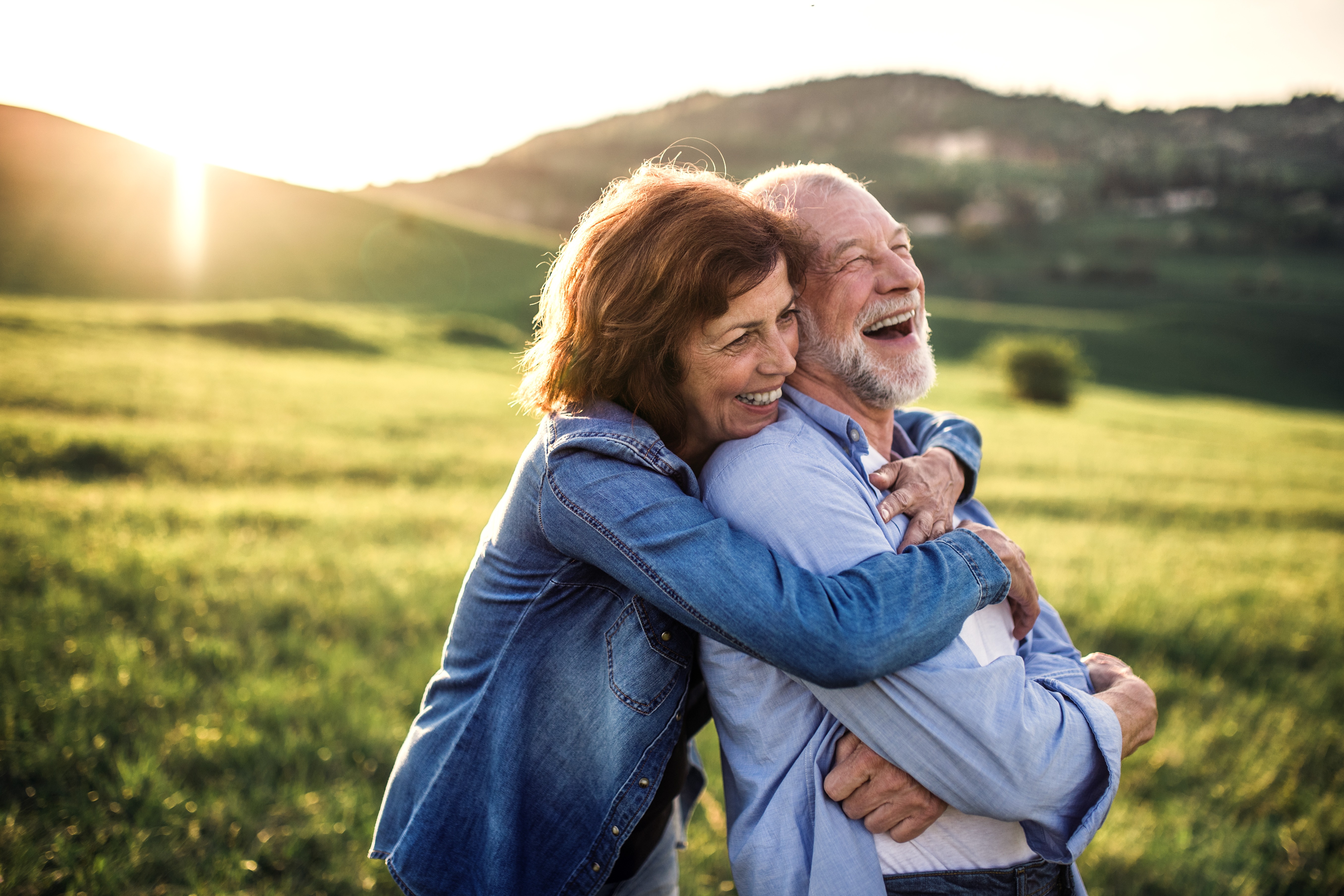 A mature couple smiling and supporting each other in a sunny meadow.