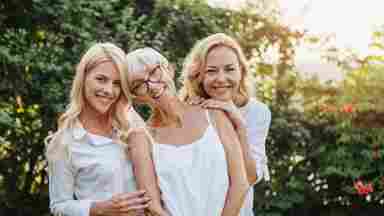 Three happy women posing closely together and smiling outdoors.