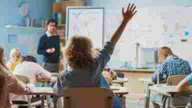 A middle school student eagerly raising a hand to answer a question during a classroom lesson with peers.