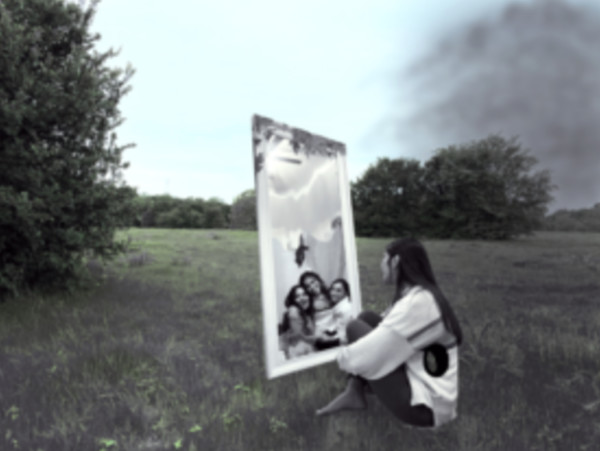 One of the 2020 Art of Kindness winners: a photograph titled Isolation, by artist Neda Ghassemi. The image shows a young person alone in a field, smoke looming in the background, as they look into a large framed portrait of a happy family.
