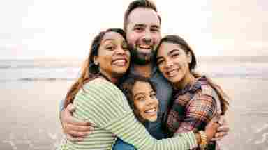 A happy, multiracial family hugging on the beach and smiling.