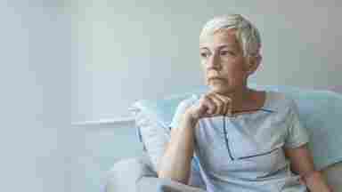 An elderly woman is thinking deeply while holding her glasses. Pensive. Older.