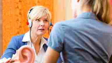 Older woman taking a hearing test with a large model of the human ear in the foreground.