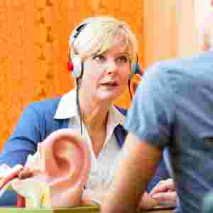 Older woman taking a hearing test with a large model of the human ear in the foreground.