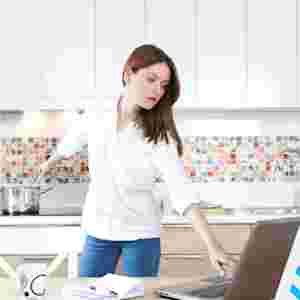 A Woman in the Kitchen Looking at the Computer Cooking; Multitasking; Distractions. IStock# 476295592.