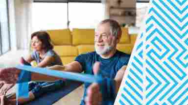 An older couple on the floor of a living room, smiling as they exercise with resistance bands. 