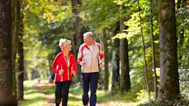 Happy elderly senior couple jogging running or walking outside on a wooded trail. Older.