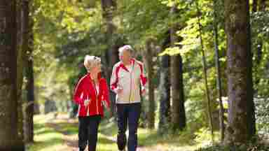 Happy elderly senior couple jogging running or walking outside on a wooded trail. Older.
