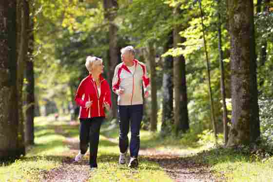 Happy elderly senior couple jogging running or walking outside on a wooded trail. Older.