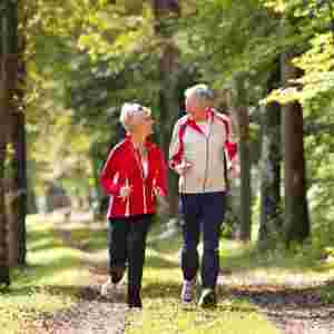 Happy elderly senior couple jogging running or walking outside on a wooded trail. Older.
