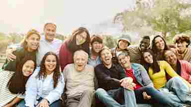 Happy multigenerational people having fun sitting on grass in a public park.
