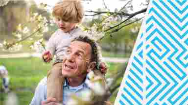 A grandfather walking beneath blossoming trees and carrying a toddler on his shoulders.