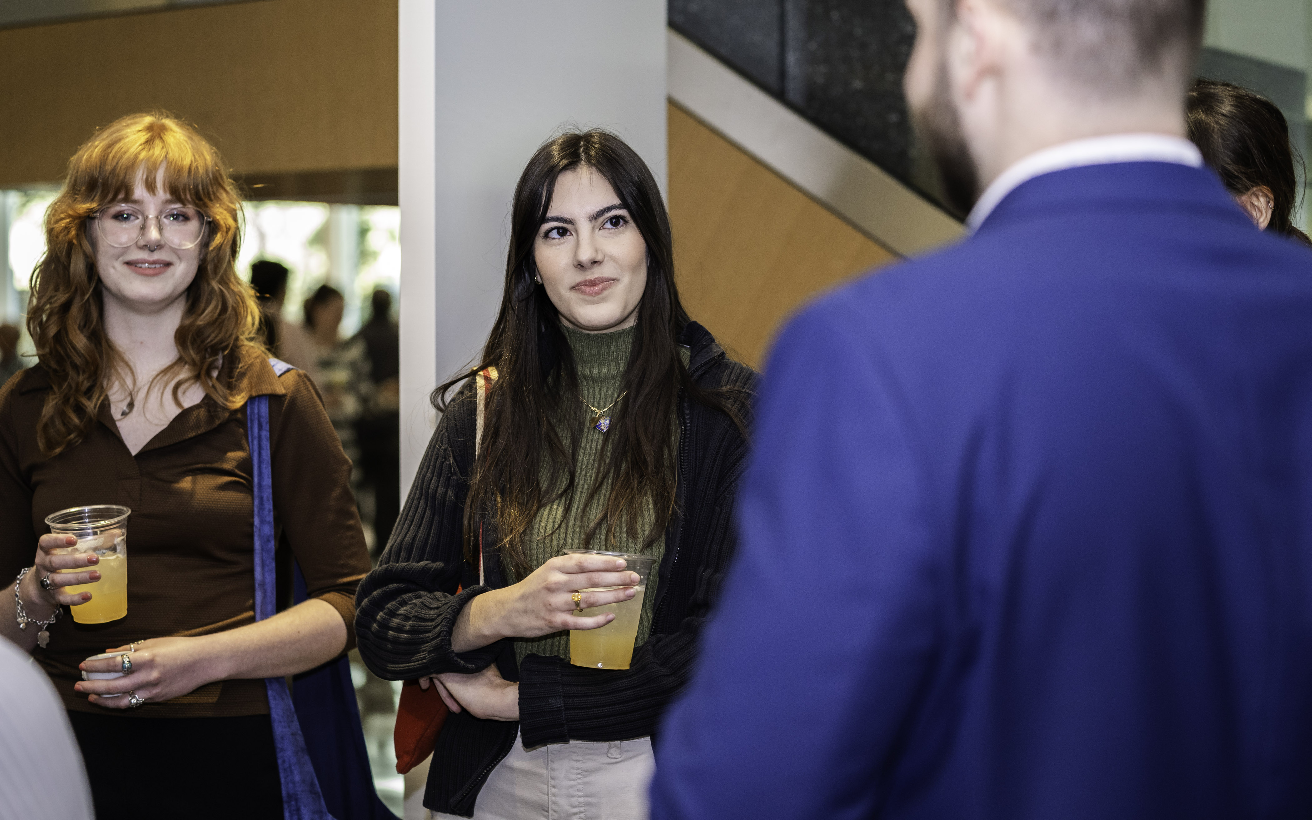 Two guests holding drinks and speaking to an event speaker in a blue suit, during a reception inside Center for BrainHealth's spacious and modern Brain Performance Institute.
